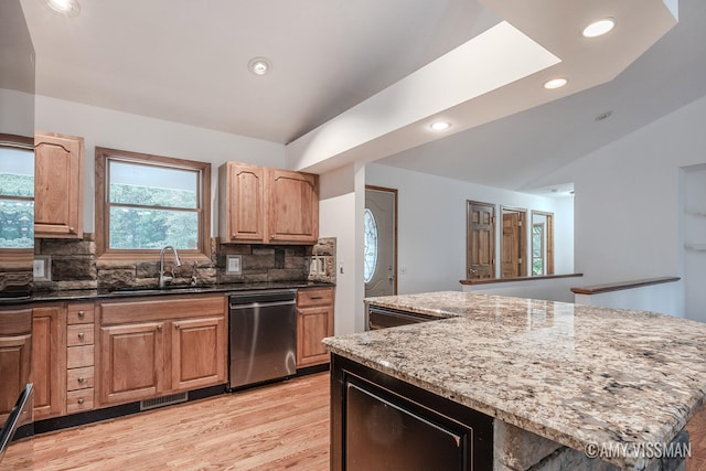 kitchen with light stone counters, backsplash, a kitchen island, stainless steel dishwasher, and sink