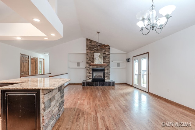 unfurnished living room featuring a stone fireplace, vaulted ceiling, light hardwood / wood-style flooring, and a notable chandelier