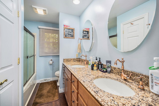 full bathroom with combined bath / shower with glass door, hardwood / wood-style flooring, vanity, and toilet