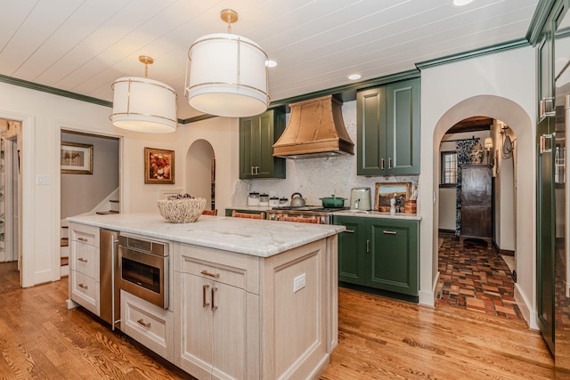 kitchen with hanging light fixtures, a kitchen island, custom range hood, decorative backsplash, and appliances with stainless steel finishes