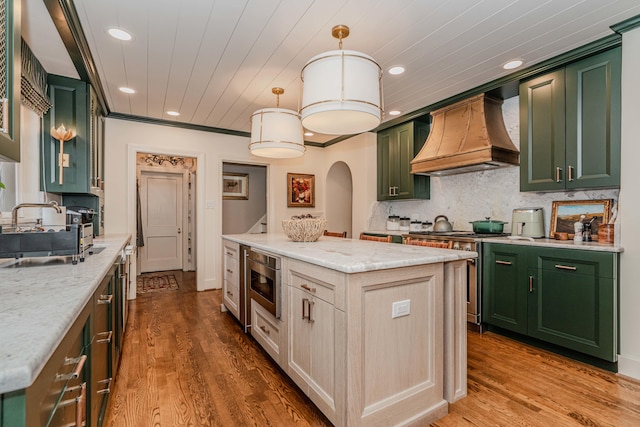 kitchen with light stone counters, a kitchen island, stainless steel appliances, custom exhaust hood, and hardwood / wood-style flooring