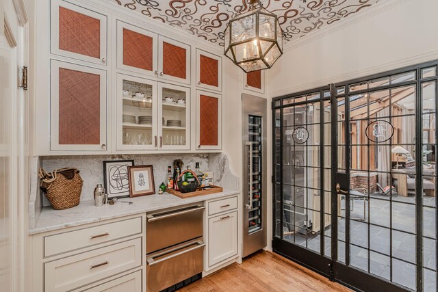 bar featuring white cabinetry, light stone counters, pendant lighting, light wood-type flooring, and ornamental molding