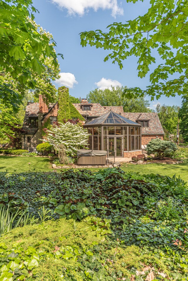 rear view of house featuring a sunroom, a hot tub, and a yard