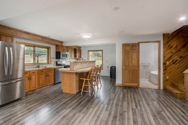 kitchen with a kitchen island, backsplash, appliances with stainless steel finishes, a breakfast bar, and dark hardwood / wood-style flooring