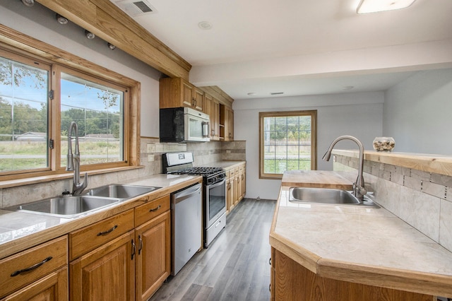 kitchen featuring sink, tasteful backsplash, a kitchen island with sink, hardwood / wood-style flooring, and appliances with stainless steel finishes