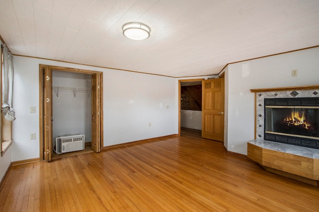 unfurnished living room featuring light wood-type flooring, crown molding, a wall unit AC, and a premium fireplace