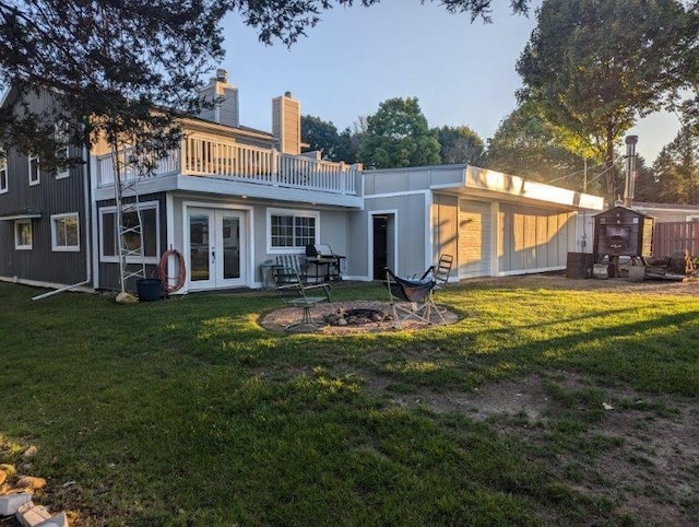 rear view of property featuring a yard, a storage unit, french doors, and a fire pit