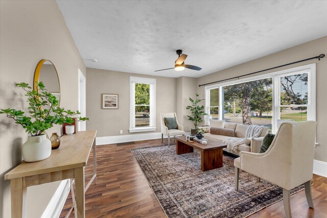 living room with a textured ceiling, ceiling fan, and dark hardwood / wood-style flooring