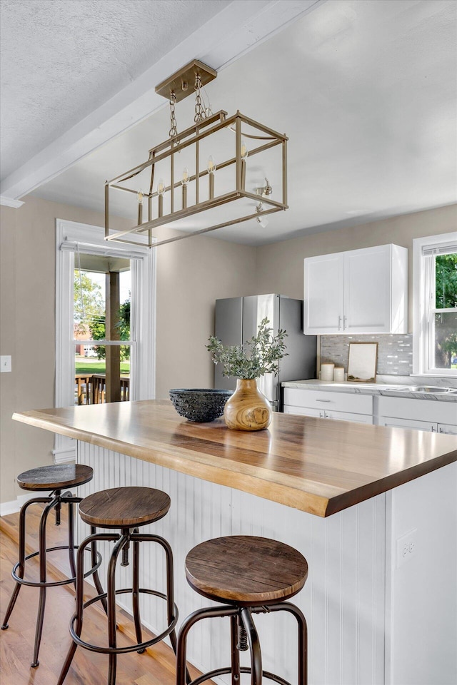 kitchen featuring white cabinets, wooden counters, light hardwood / wood-style flooring, stainless steel refrigerator, and a kitchen breakfast bar