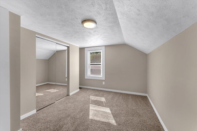 additional living space with vaulted ceiling, a textured ceiling, and carpet flooring