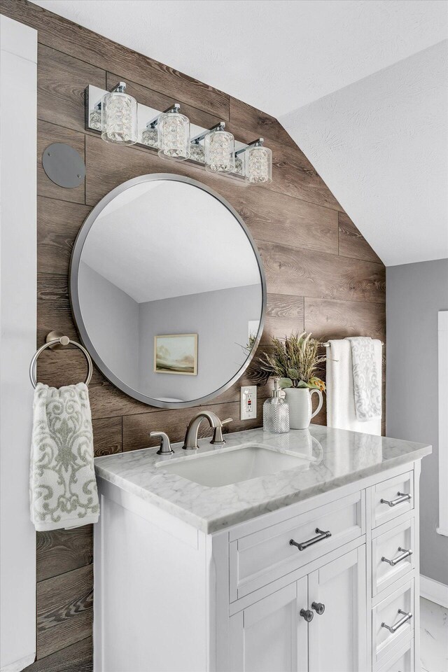 bathroom featuring lofted ceiling, wood walls, and vanity