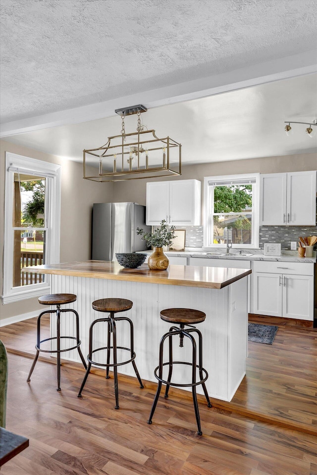 kitchen featuring a wealth of natural light, white cabinetry, hardwood / wood-style flooring, and stainless steel fridge