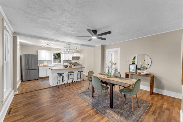 dining area featuring ceiling fan, hardwood / wood-style flooring, crown molding, and a textured ceiling