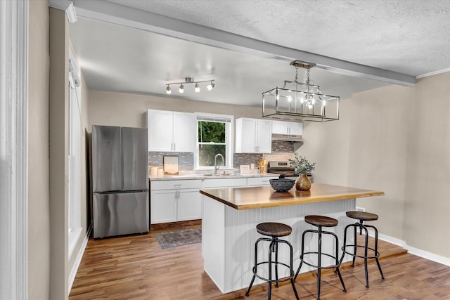 kitchen featuring hanging light fixtures, white cabinets, stainless steel appliances, a center island, and hardwood / wood-style flooring