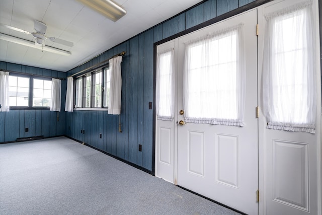 carpeted entrance foyer featuring wood walls, ceiling fan, and a wealth of natural light