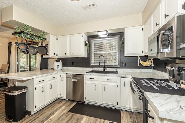 kitchen featuring light hardwood / wood-style floors, sink, white cabinetry, kitchen peninsula, and stainless steel appliances