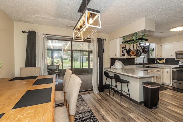 kitchen with sink, kitchen peninsula, white cabinetry, hardwood / wood-style flooring, and appliances with stainless steel finishes