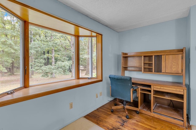 office area with a textured ceiling, built in desk, and hardwood / wood-style floors