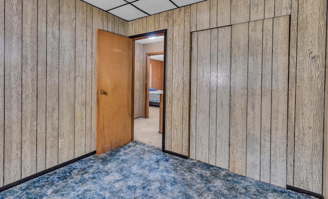 unfurnished bedroom with a drop ceiling, wood walls, dark carpet, and a closet