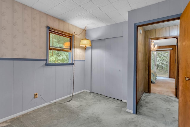 unfurnished bedroom featuring light carpet, wood walls, and multiple windows