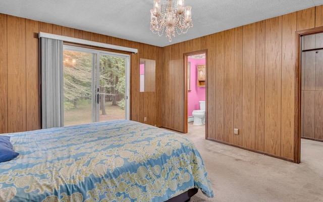 bedroom with access to outside, light colored carpet, ensuite bath, and wood walls