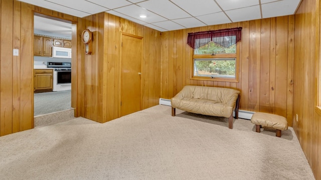 sitting room featuring wooden walls, baseboard heating, carpet floors, and a paneled ceiling