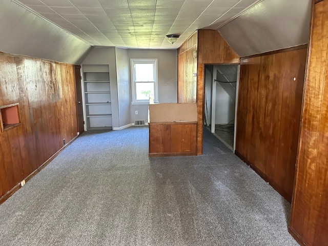 additional living space featuring dark carpet, lofted ceiling, and wood walls