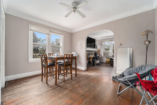 dining room featuring ceiling fan, a stone fireplace, crown molding, and dark hardwood / wood-style flooring