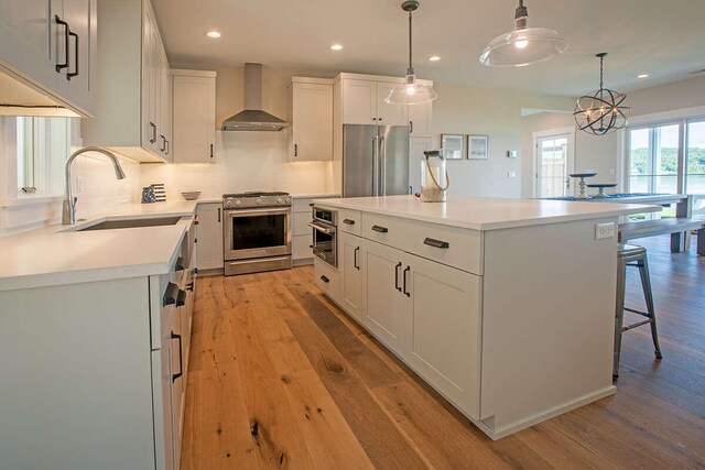 kitchen with light hardwood / wood-style floors, white cabinetry, stainless steel appliances, a center island, and wall chimney range hood