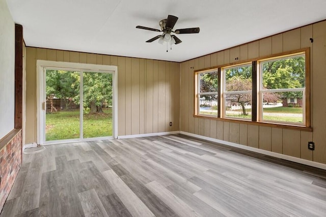 unfurnished room with light wood-type flooring, ceiling fan, a healthy amount of sunlight, and wooden walls