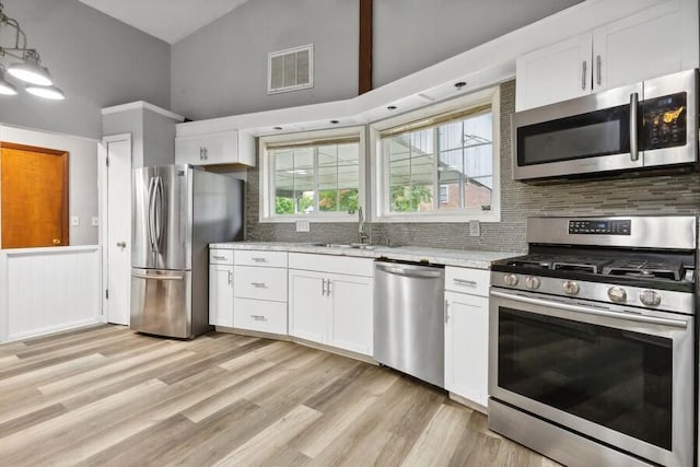 kitchen featuring appliances with stainless steel finishes, white cabinets, high vaulted ceiling, backsplash, and sink