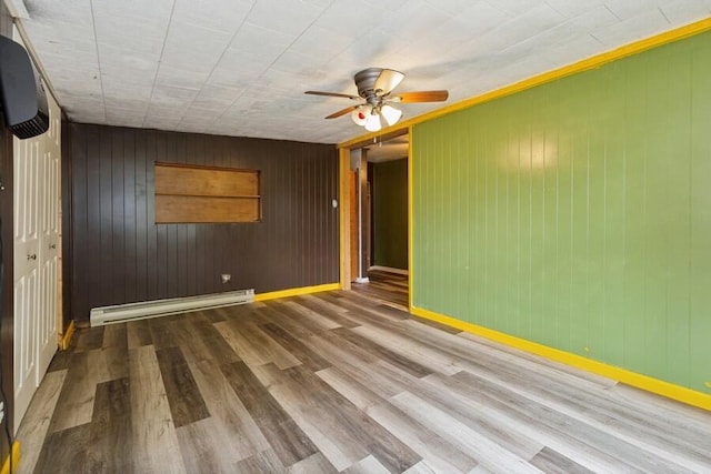 empty room featuring a baseboard heating unit, wood-type flooring, a wall unit AC, wood walls, and ceiling fan