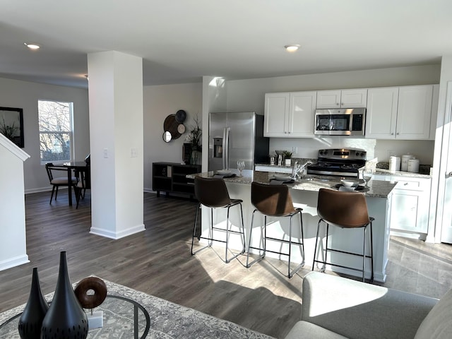 kitchen with stainless steel appliances, white cabinets, stone counters, and a kitchen bar