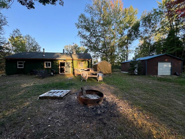 rear view of house with a yard, an outdoor structure, and a fire pit