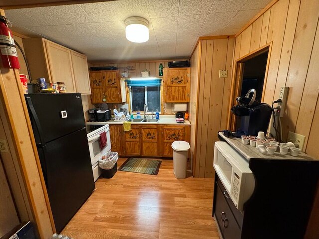 kitchen with light wood-type flooring, black fridge, sink, wood walls, and white range with electric stovetop