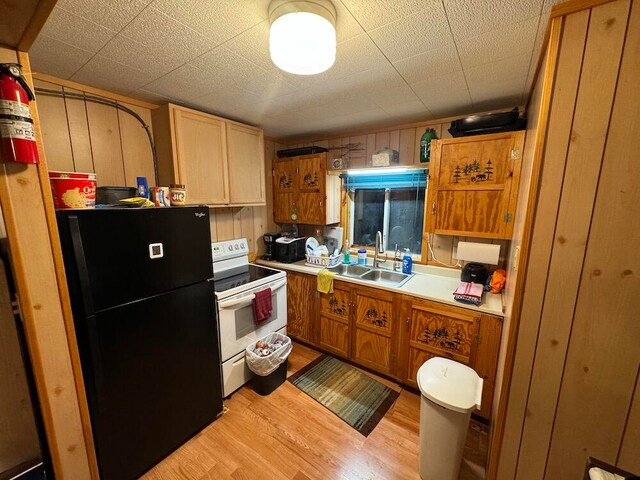 kitchen with light wood-type flooring, wooden walls, white range with electric cooktop, black fridge, and sink