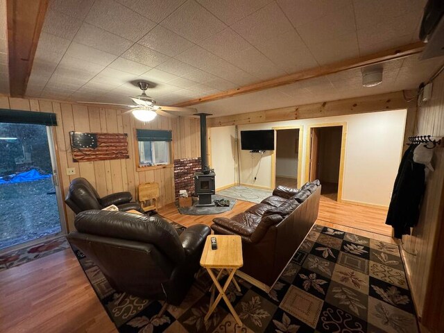 living room with wood-type flooring, wood walls, ceiling fan, and a wood stove