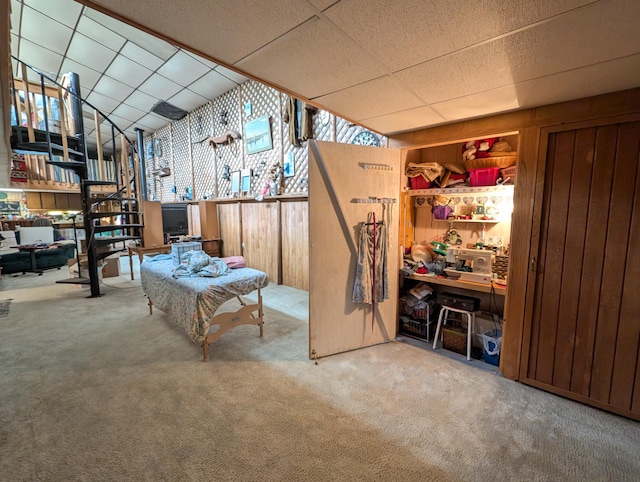 interior space featuring wooden walls, a drop ceiling, and carpet flooring