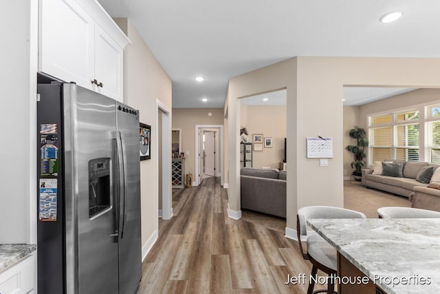 kitchen featuring light wood-type flooring, stainless steel fridge, white cabinetry, and light stone countertops