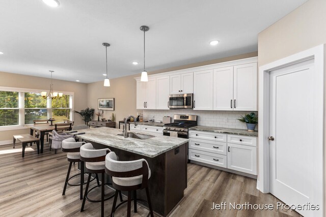 kitchen featuring sink, white cabinets, stainless steel appliances, a center island with sink, and decorative light fixtures