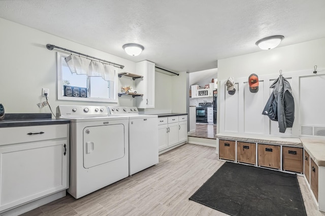 laundry area featuring light wood-type flooring, cabinets, a textured ceiling, and independent washer and dryer