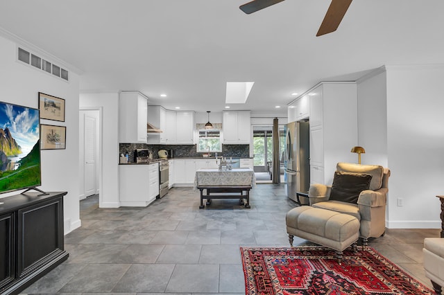 living room with ceiling fan, a skylight, ornamental molding, sink, and tile patterned flooring