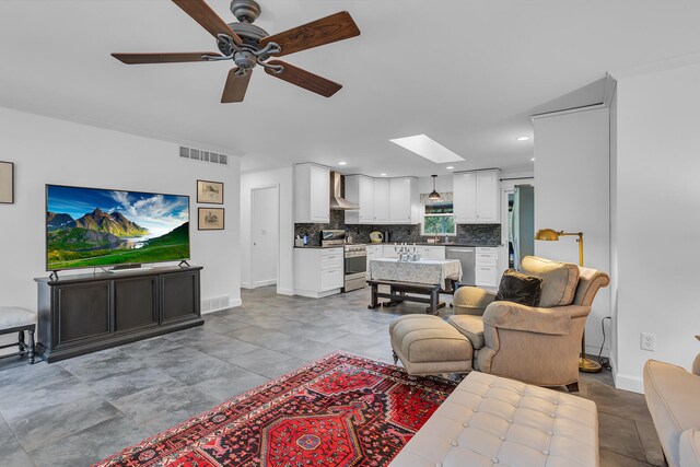 living room featuring ceiling fan, a skylight, and sink