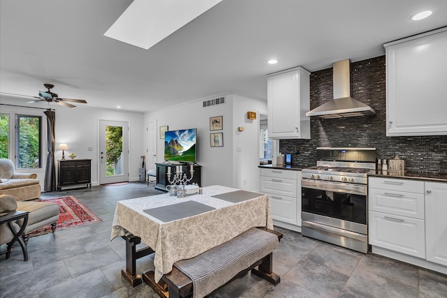 kitchen with wall chimney exhaust hood, white cabinets, stainless steel gas range oven, and plenty of natural light