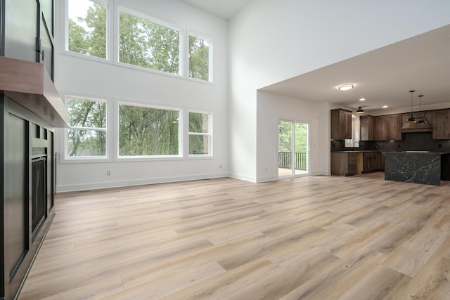 unfurnished living room with light wood-type flooring, a healthy amount of sunlight, a high ceiling, and sink