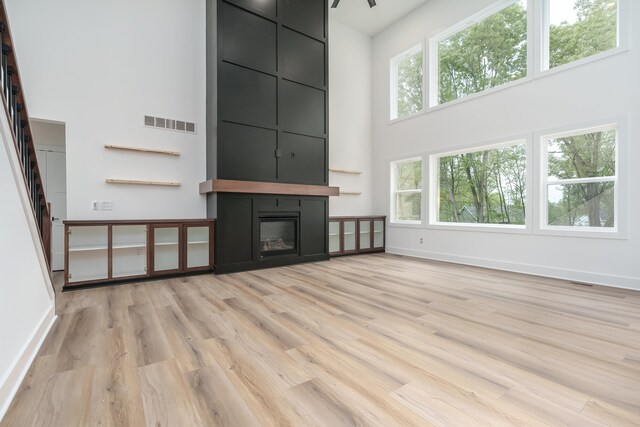 unfurnished living room with plenty of natural light, a fireplace, light hardwood / wood-style flooring, and a towering ceiling