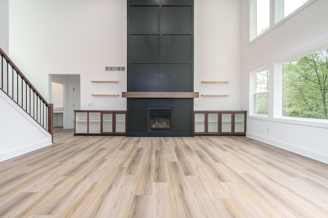 unfurnished living room featuring a towering ceiling, a wealth of natural light, and light hardwood / wood-style flooring