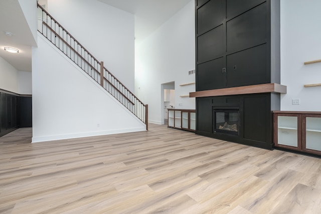 unfurnished living room with a towering ceiling, light hardwood / wood-style floors, and a fireplace