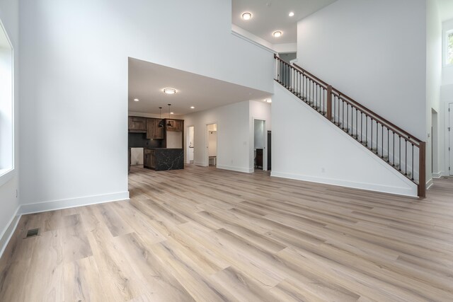 unfurnished living room featuring a high ceiling and light hardwood / wood-style floors