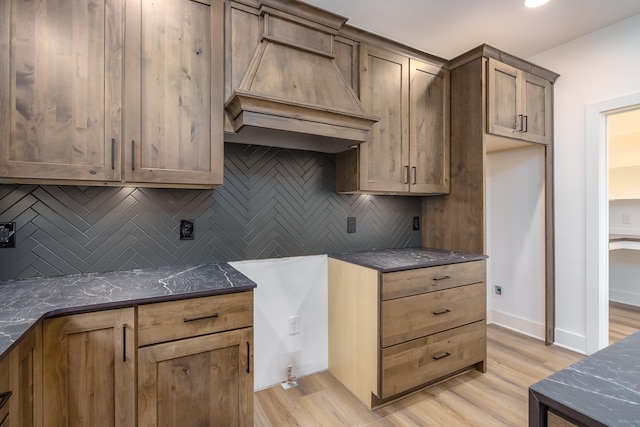 kitchen with dark stone counters, light wood-type flooring, decorative backsplash, and custom exhaust hood